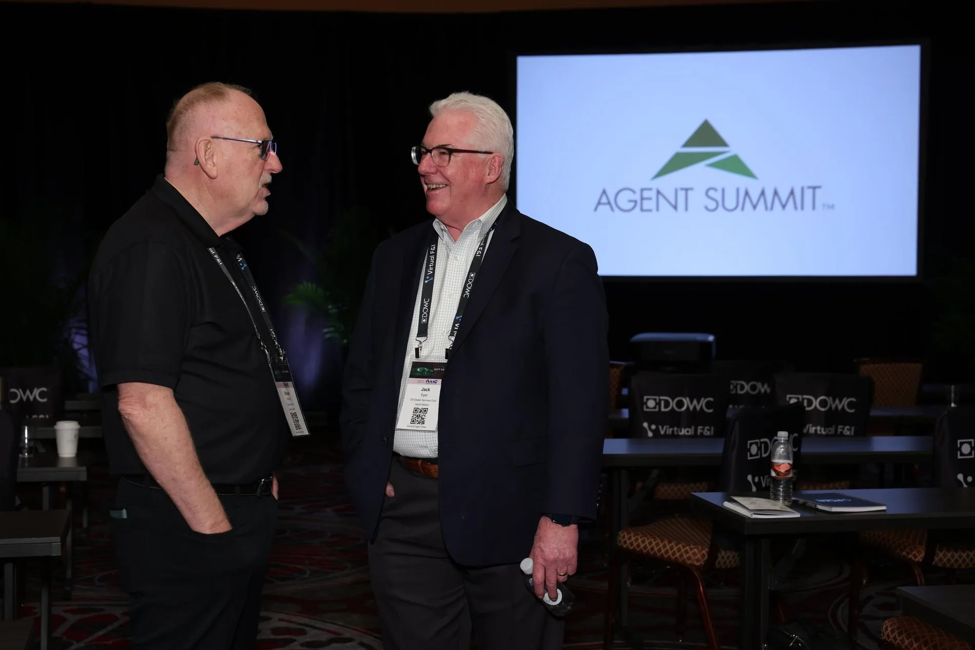Two general agents talking in the main room at Agent Summit; the event logo is on the screen behind them
